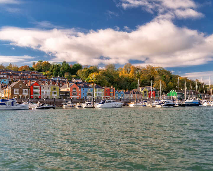 Colorful buildings line a waterfront at Dartmouth with boats in the water, under a blue sky with clouds.