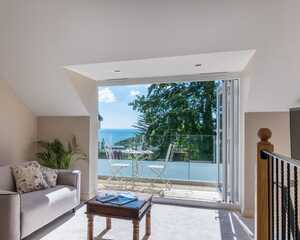 Room at Orestone Manor with a sofa and a view of trees and the coast through large glass doors.